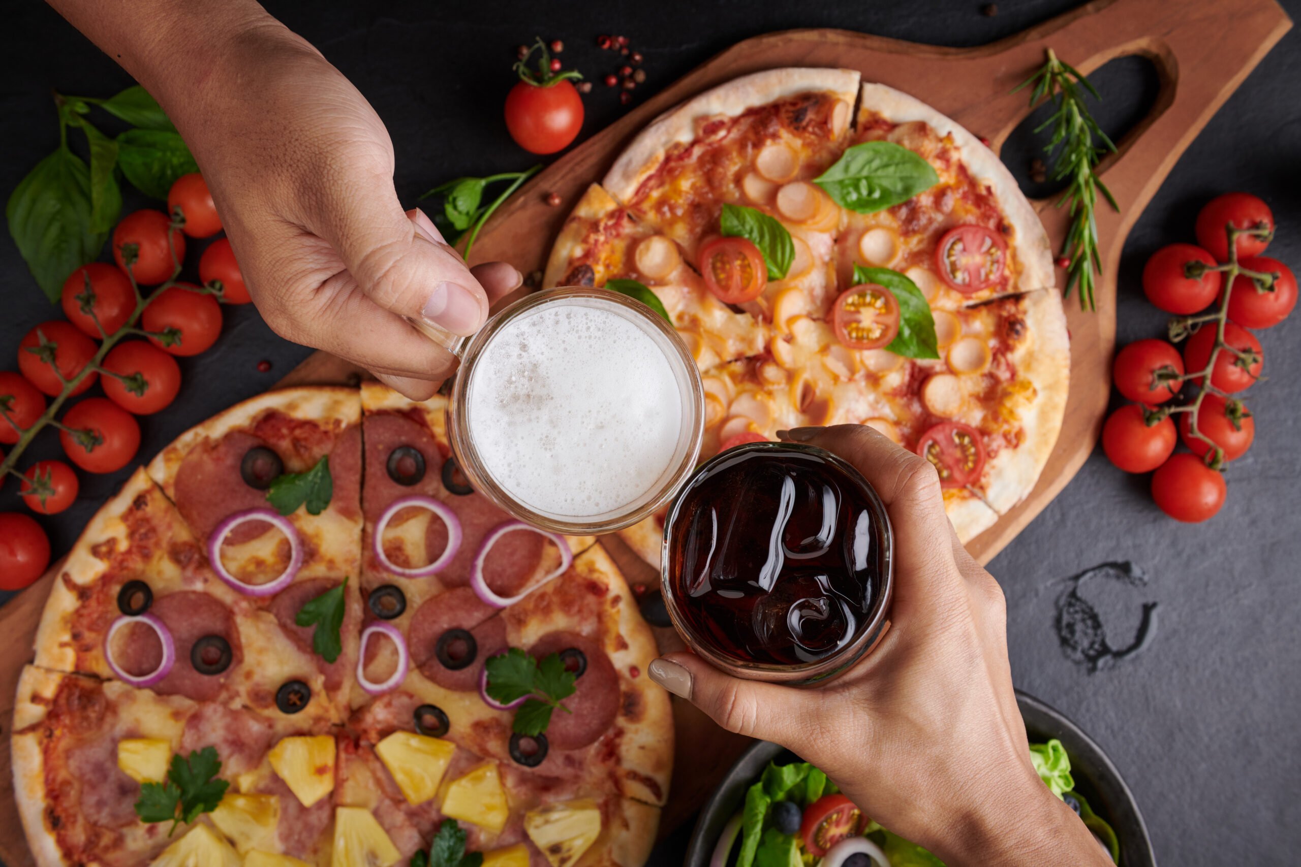 Family or friends having pizza party dinner. Flat-lay of people Family or friends having pizza party dinner. Flat-lay of people clinking glasses with drink over rustic dark stone table with various kinds of Italian pizza, top view. Fast food lunch, celebration