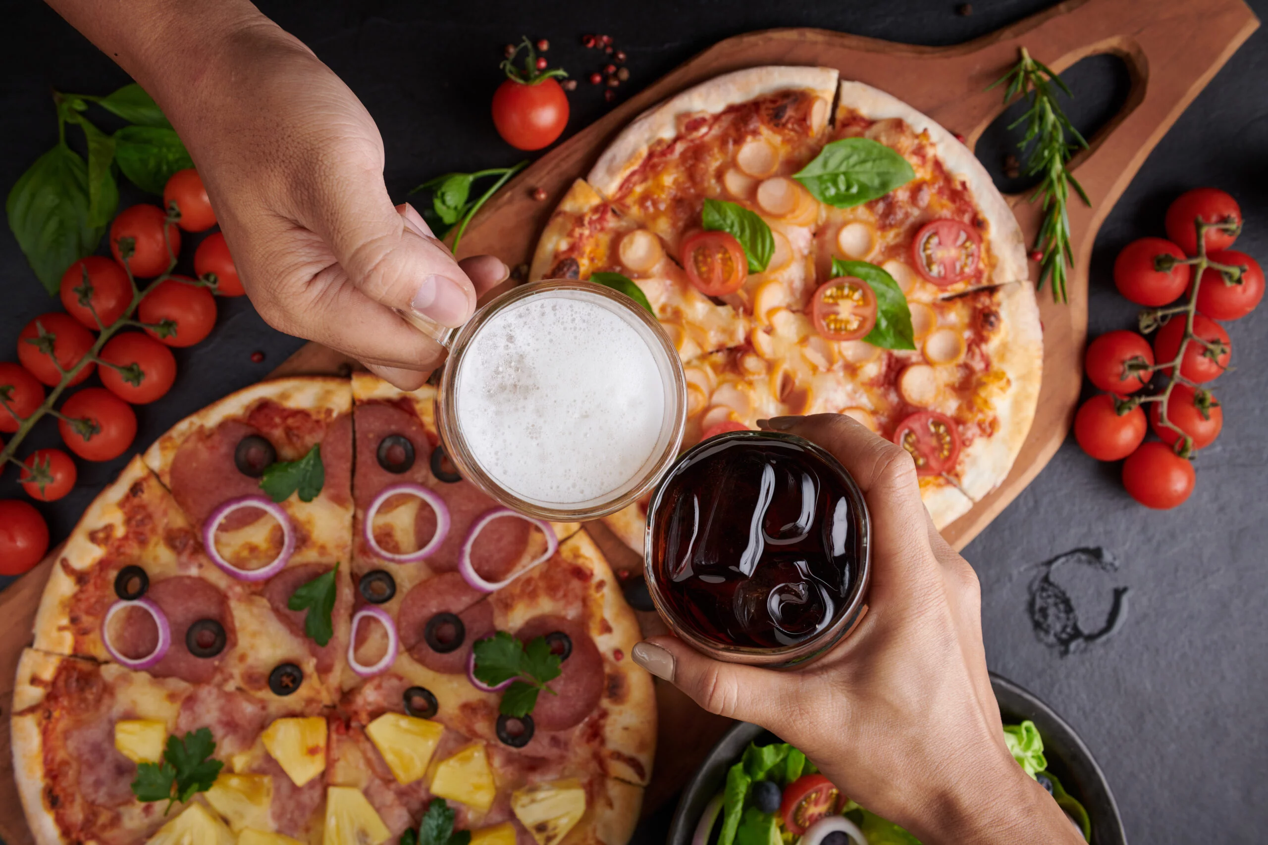 Family or friends having pizza party dinner. Flat-lay of people Family or friends having pizza party dinner. Flat-lay of people clinking glasses with drink over rustic dark stone table with various kinds of Italian pizza, top view. Fast food lunch, celebration
